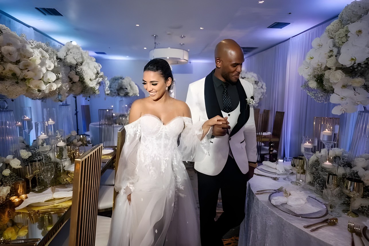 Bride and groom beside a wedding tablescape with tall white florals, gold chairs and candlelight by Sharp Designs