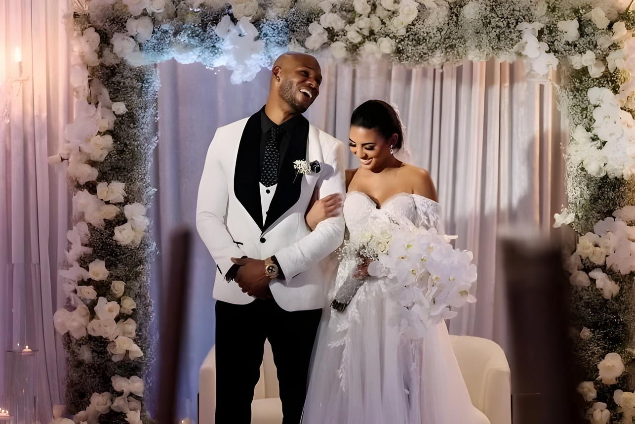 Bride and groom beneath a white floral wedding arch with baby's breath and roses by Sharp Designs