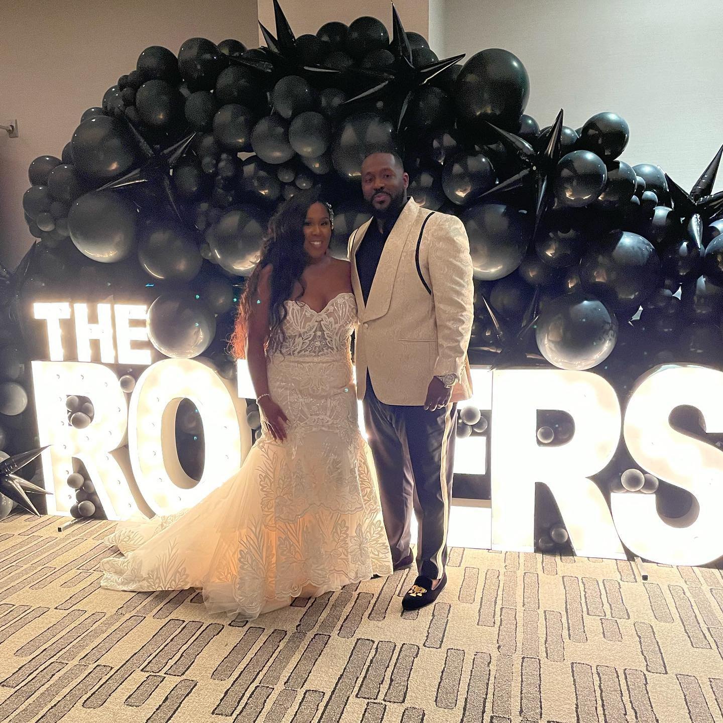 Bride and groom in front of a black balloon wall and lit marquee letters spelling The Roziers, wedding decor by Sharp Designs